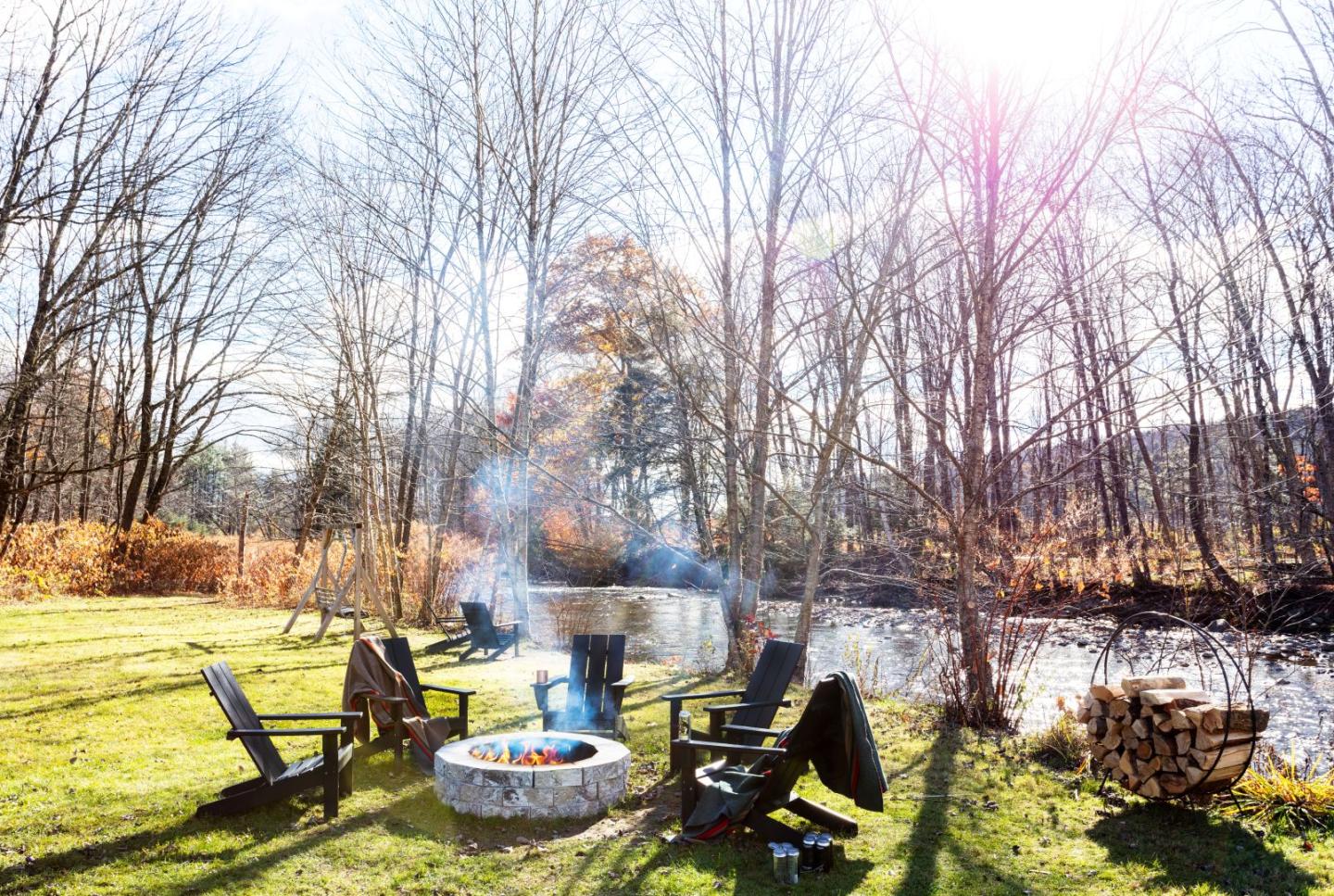 Chairs around a fire pit beside a river in a wooded area.