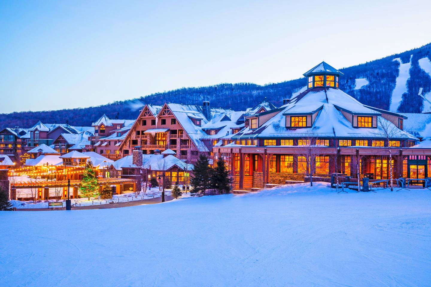 Snowy ski resort with warm lights and mountains in the background.