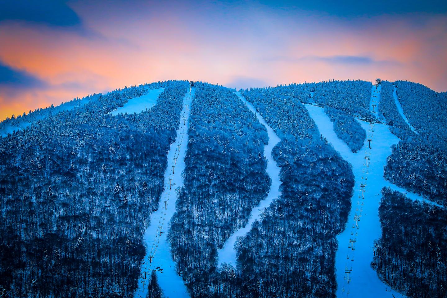 Snow-covered ski slopes on a mountain at sunset.