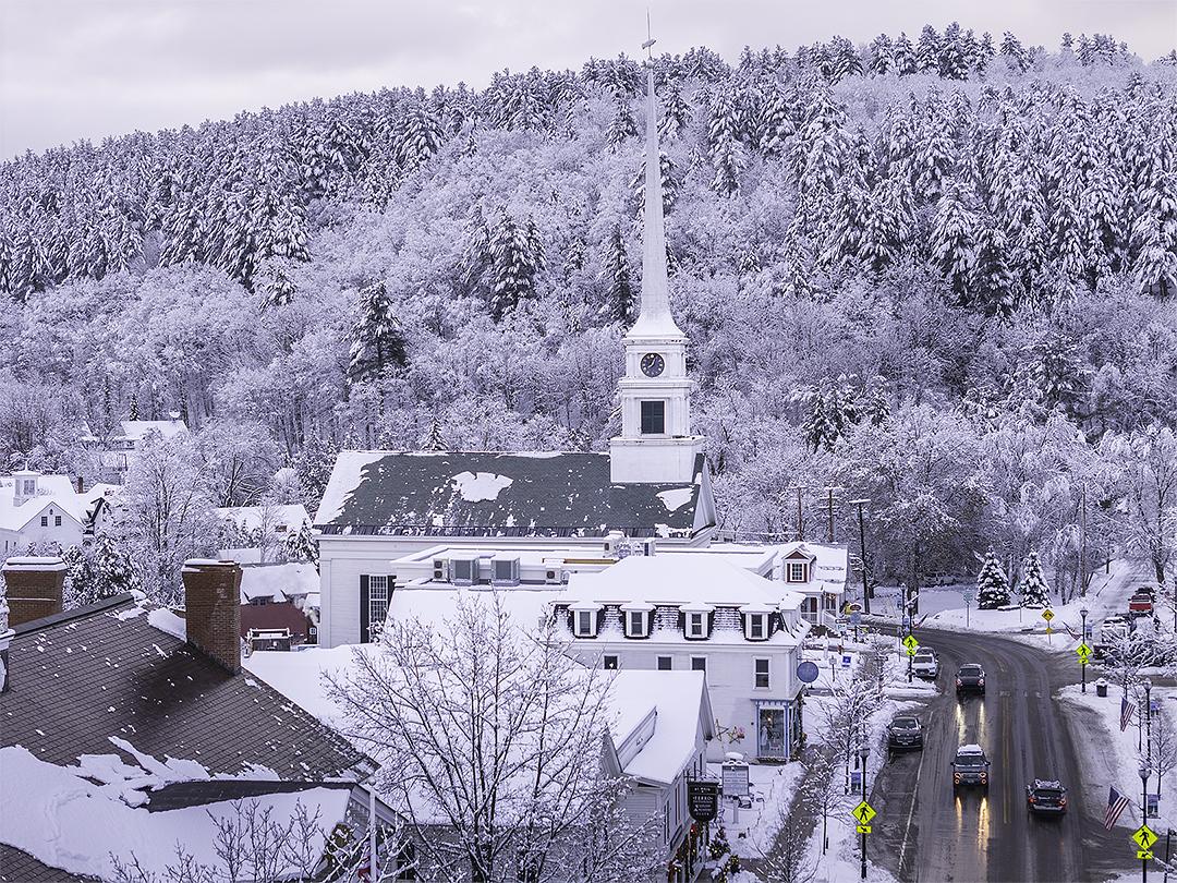 Snow-covered town with a church steeple and cars on a winter road.