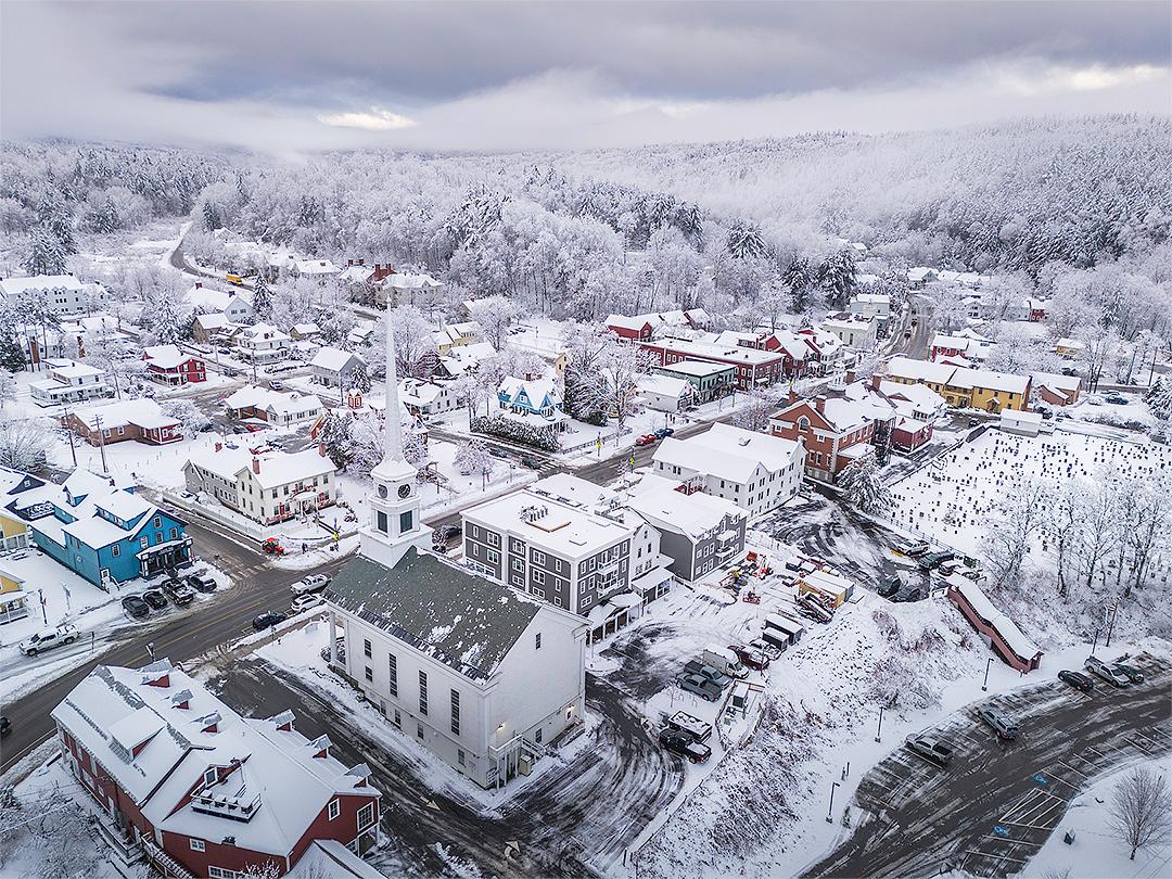 Snow-covered town with colorful houses and a church, surrounded by snowy trees.
