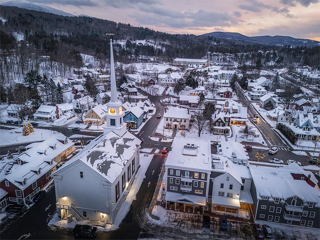 Snow-covered town at twilight, church steeple in foreground.