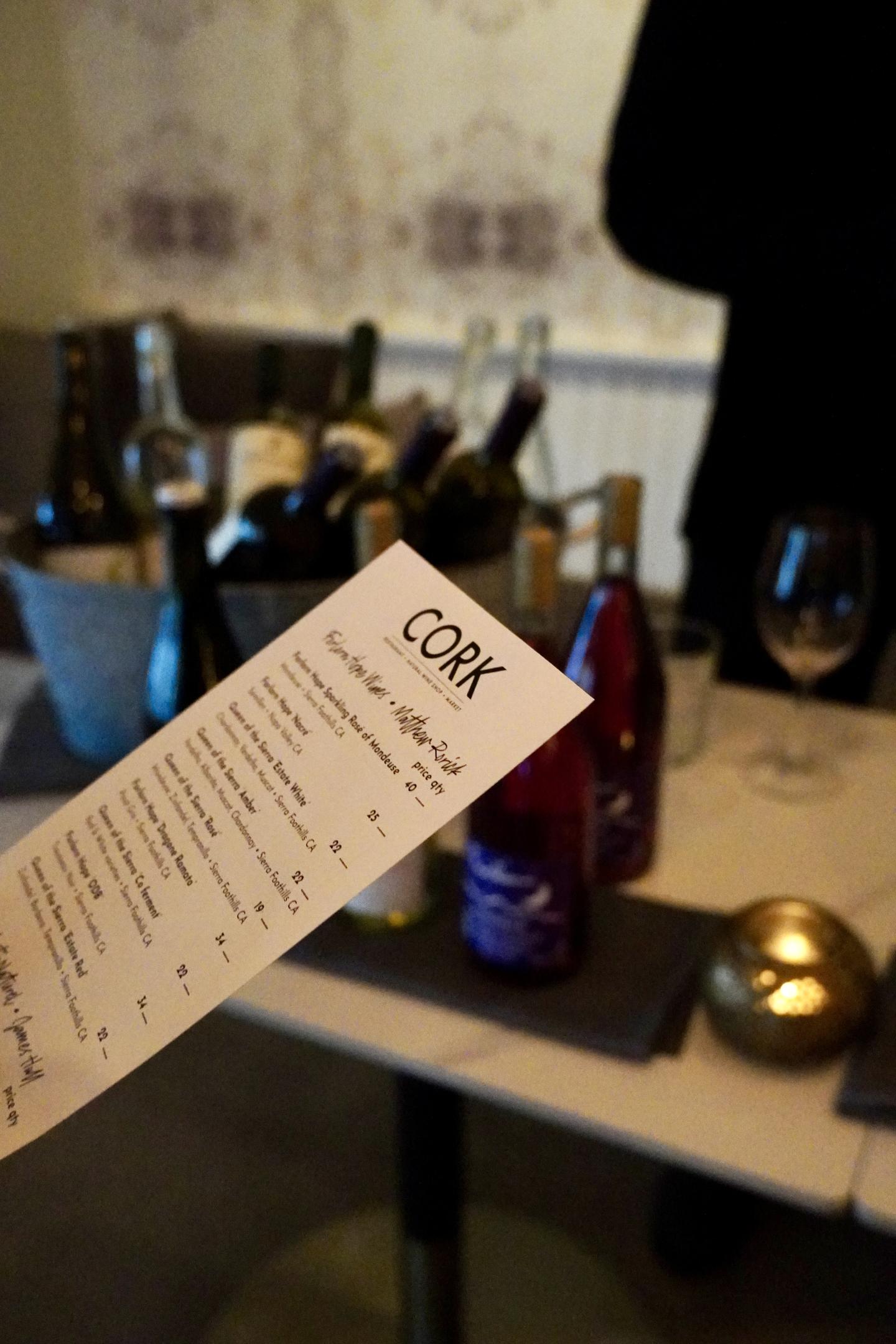 Wine menu held in focus with bottles and glasses blurred in the background.