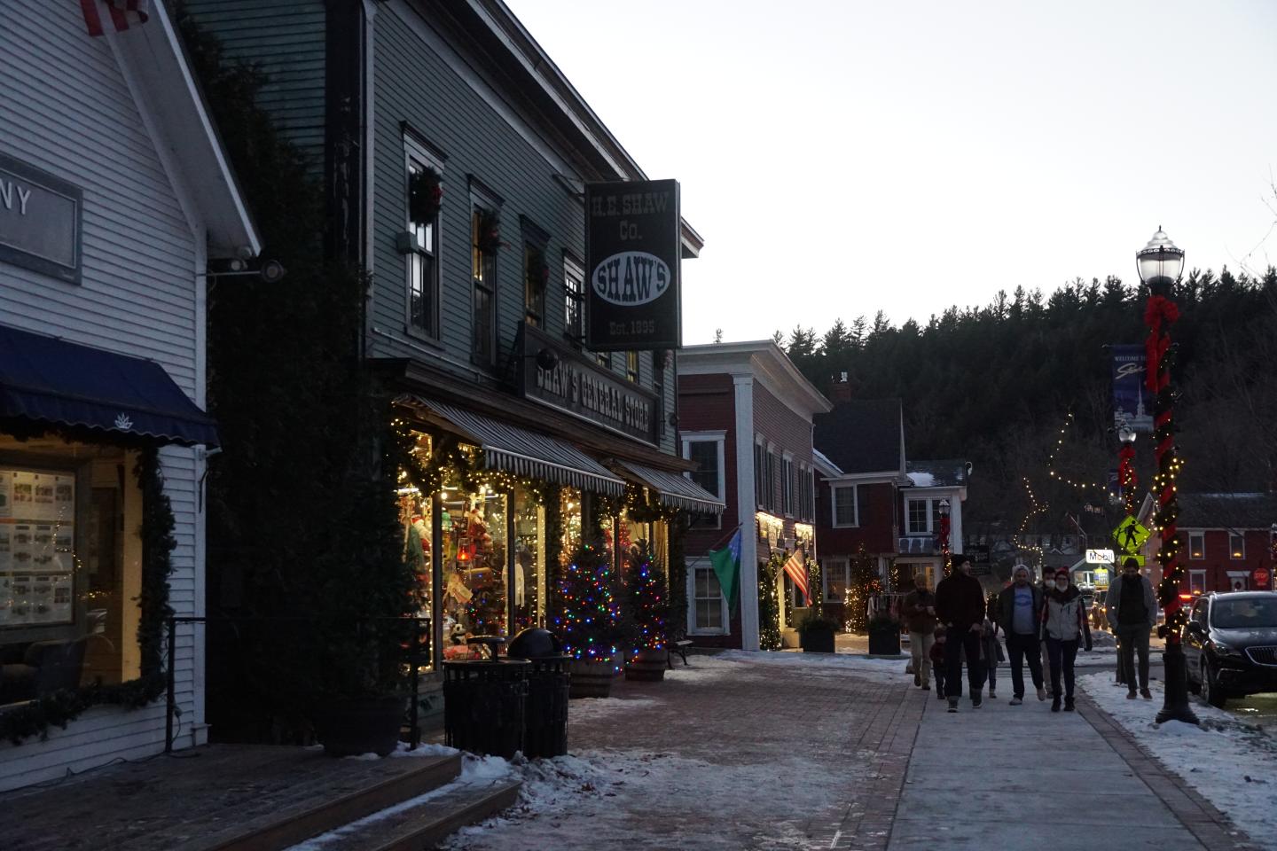 Snowy street in a small town with festive lights and people walking.