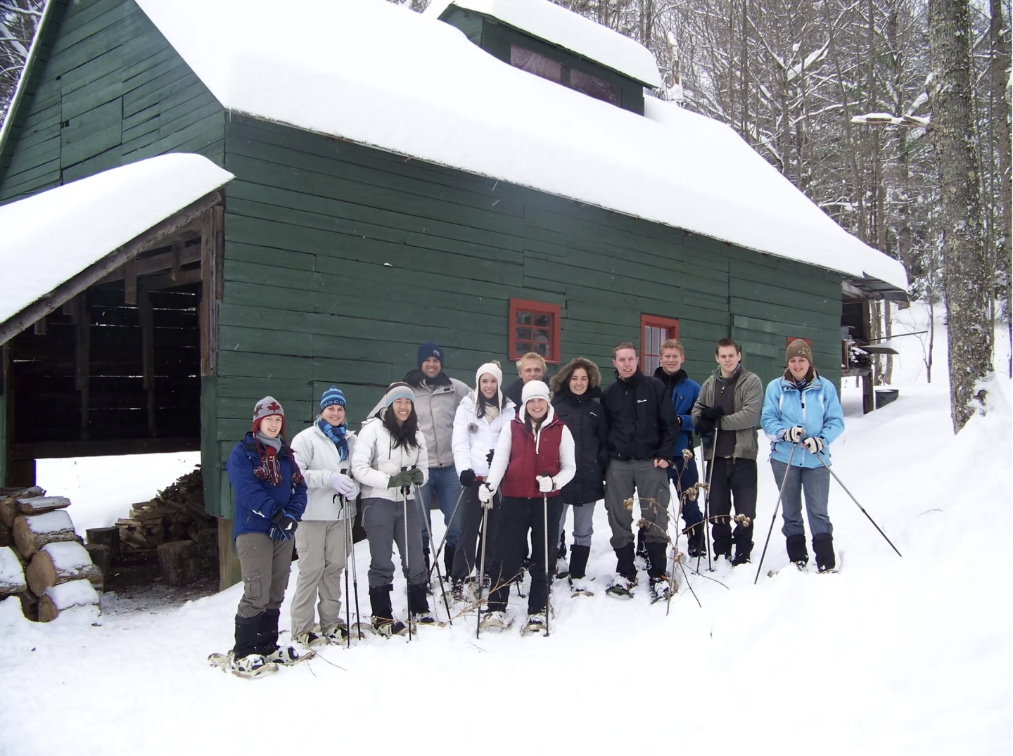 Group of people in winter gear standing in snow by a green cabin.