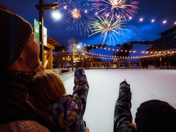 Family watching colorful fireworks in a winter setting, pointing at the sky.