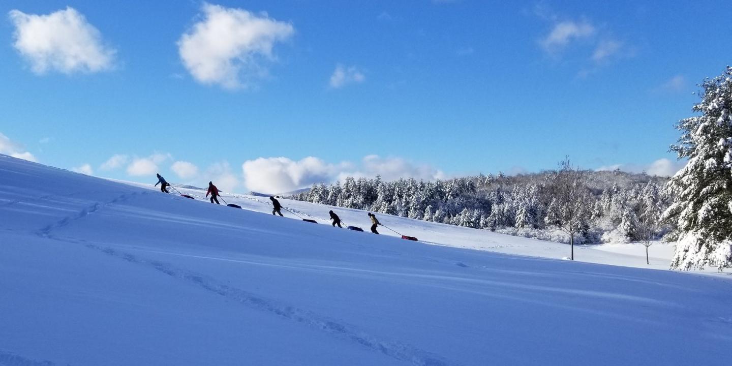 People sledding down a snowy hill under a clear blue sky.