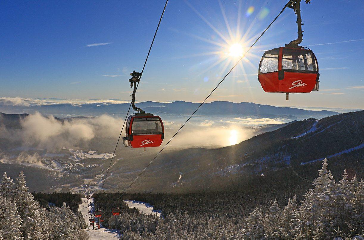 Red cable cars over a snowy mountain landscape with a bright sun and clear blue sky.