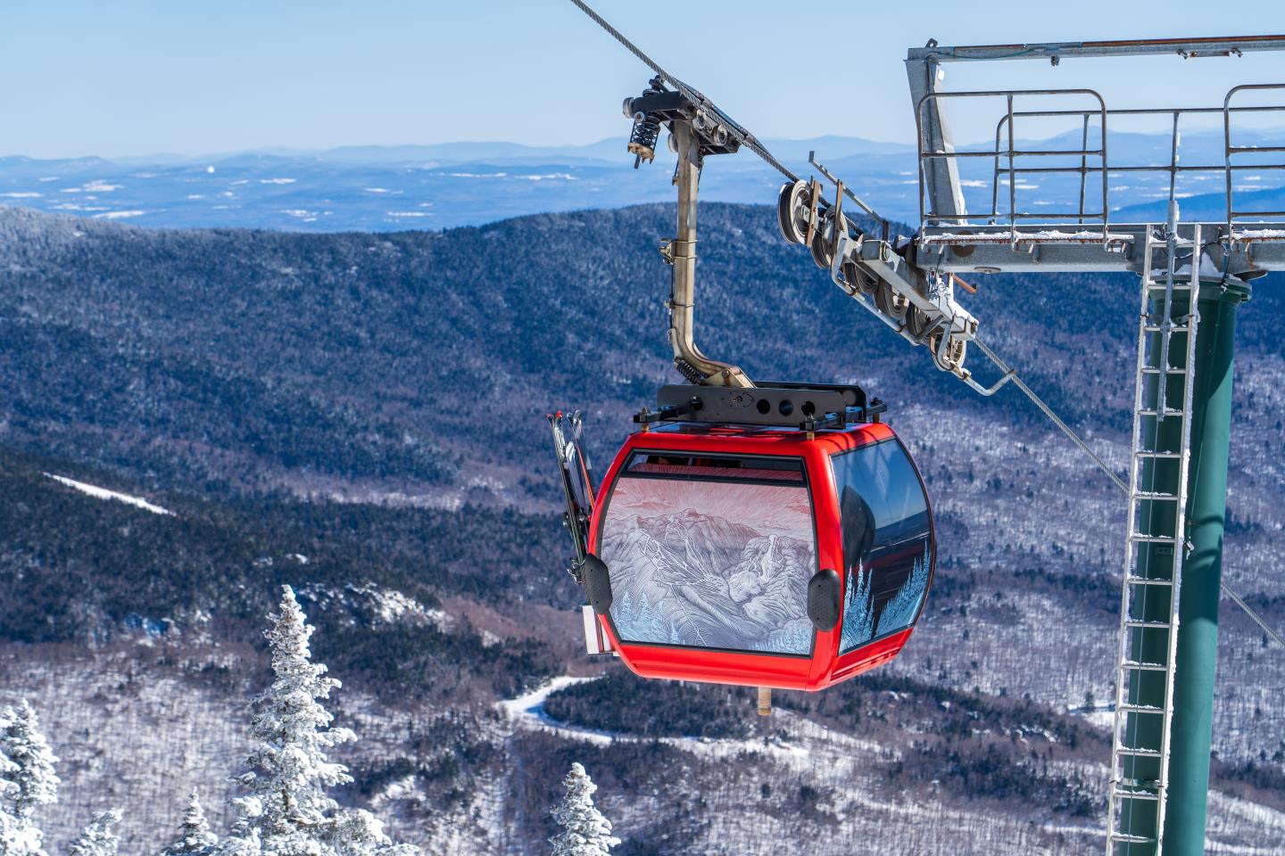 Red ski gondola in snowy mountain landscape with blue sky.