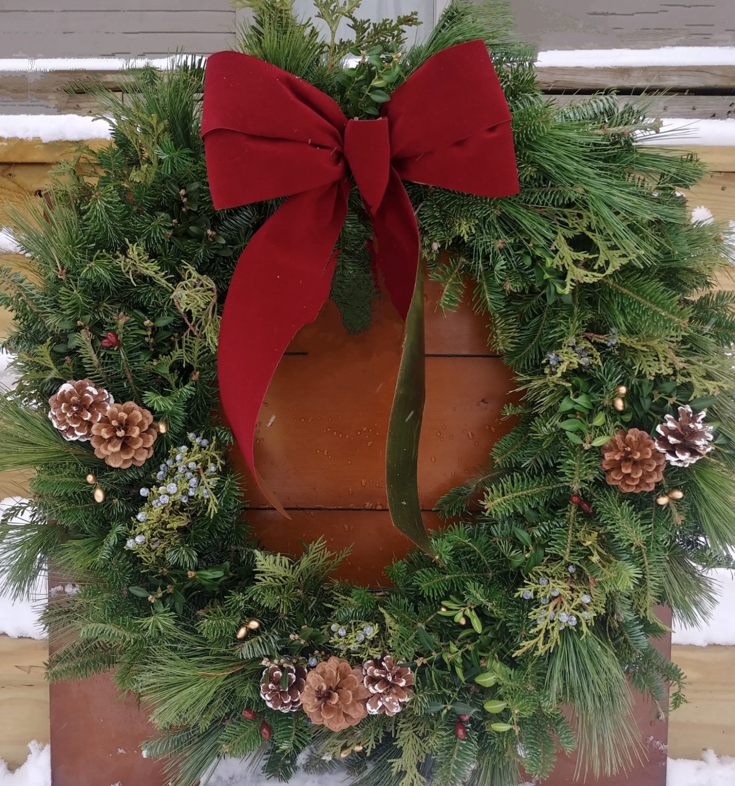 Festive wreath with a red bow, pinecones, greenery, and snow background.