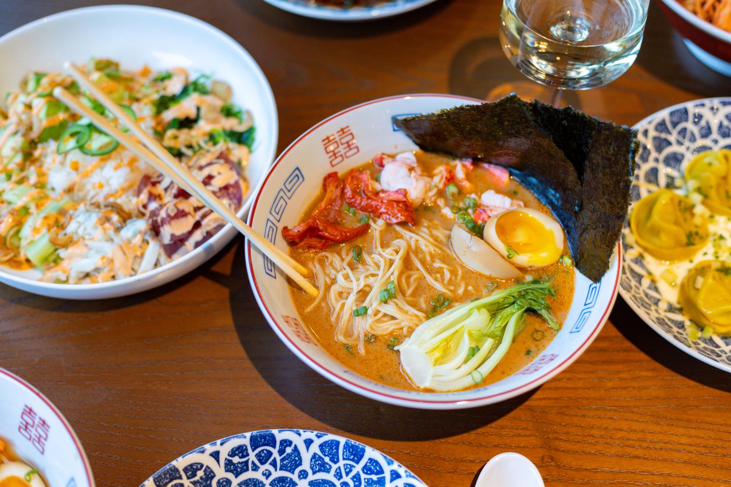 Bowl of ramen with egg, seaweed, and vegetables on a wooden table.
