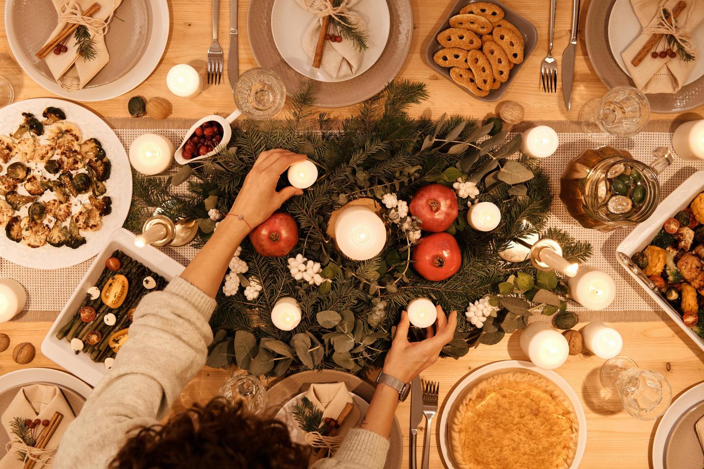 Elegant table setting with candles, greenery, red apples, and various dishes.
