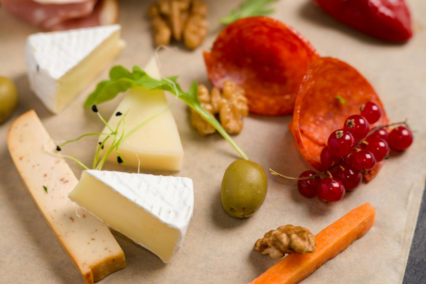 Cheese, nuts, olives, and sliced meat on parchment paper.