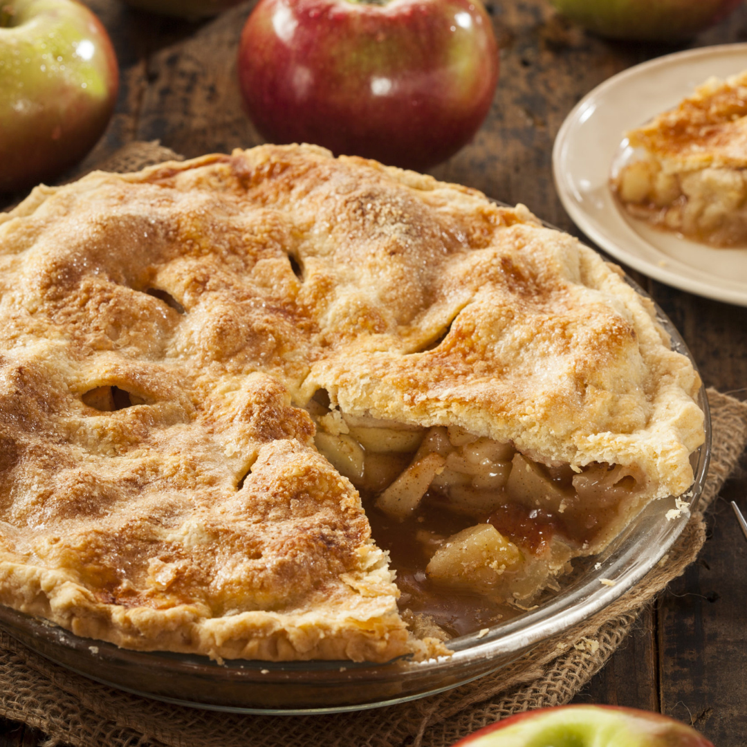 Golden-brown apple pie with a slice missing, surrounded by fresh apples.