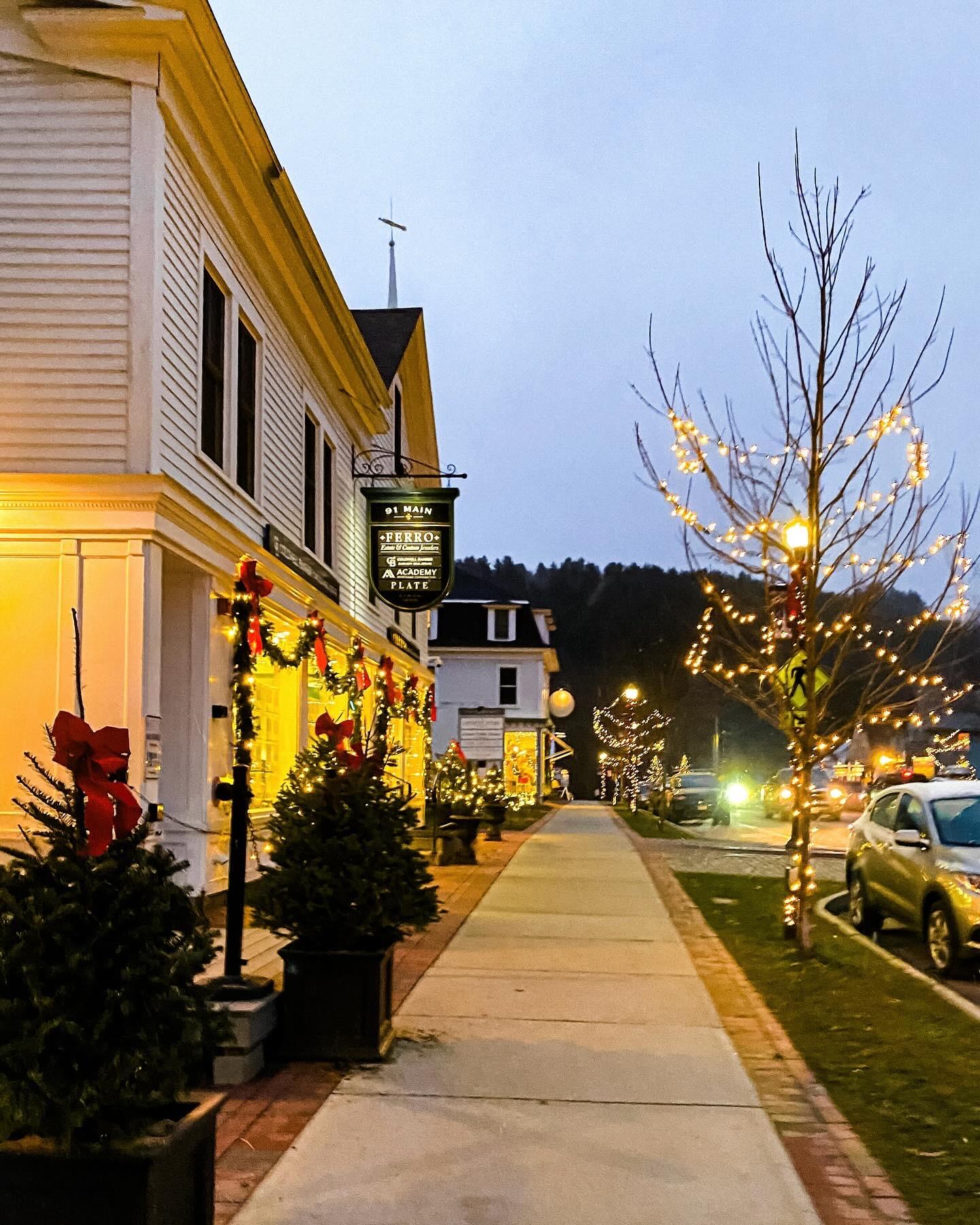 Festive street with lit trees and decorated buildings at dusk.