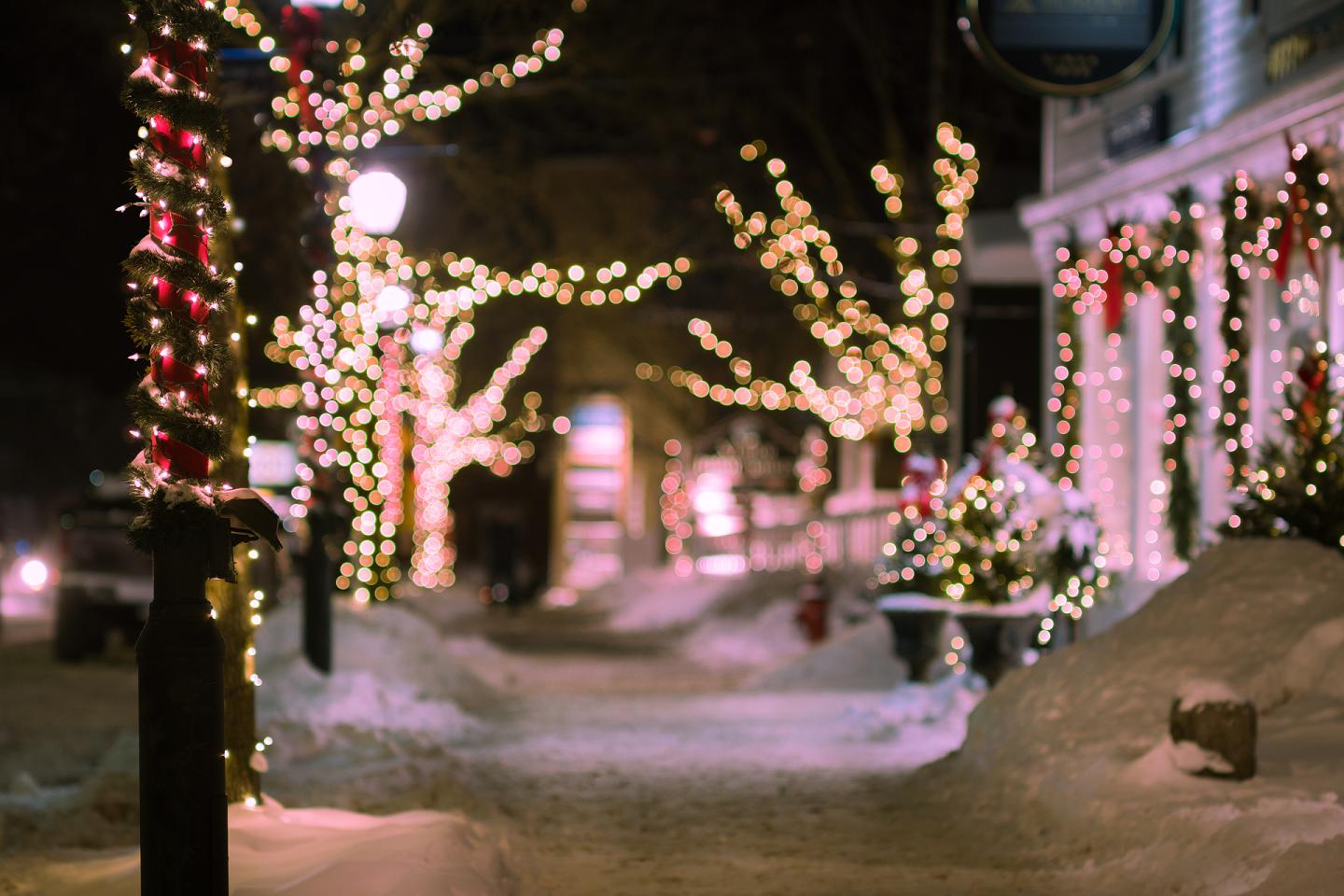 Festive street with snow-covered sidewalks and trees wrapped in sparkling lights.