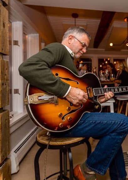 Man playing a sunburst guitar in a cozy cafe.