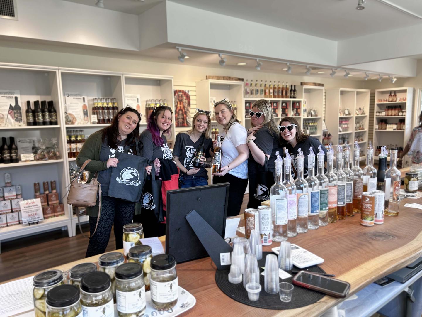 Group of people smiling behind a counter with bottles and product by smugglers notch distillery displayed.