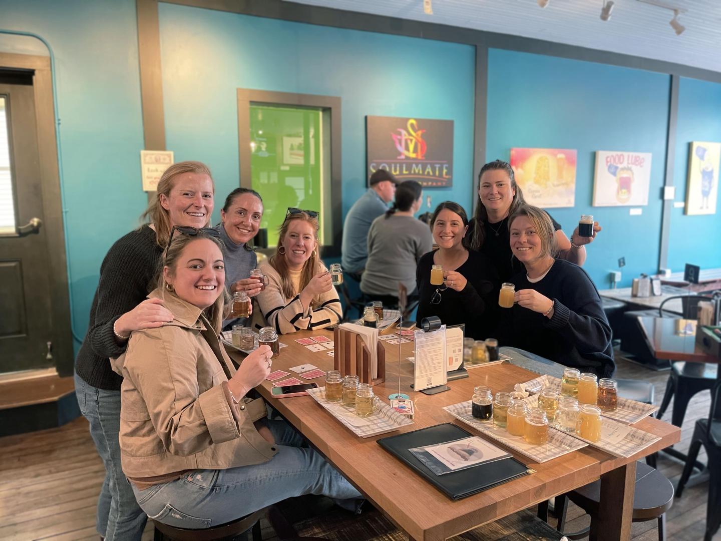 Group of people smiling, seated indoors at soulmate brewery.