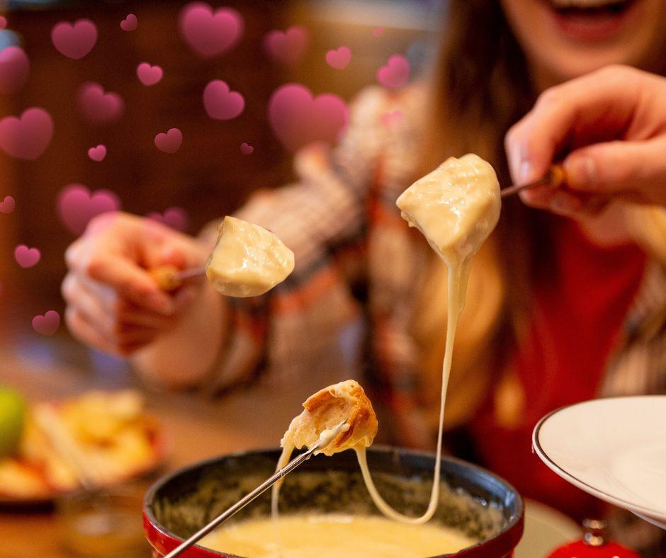 Cheese fondue with bread cubes on skewers, pink hearts in background.