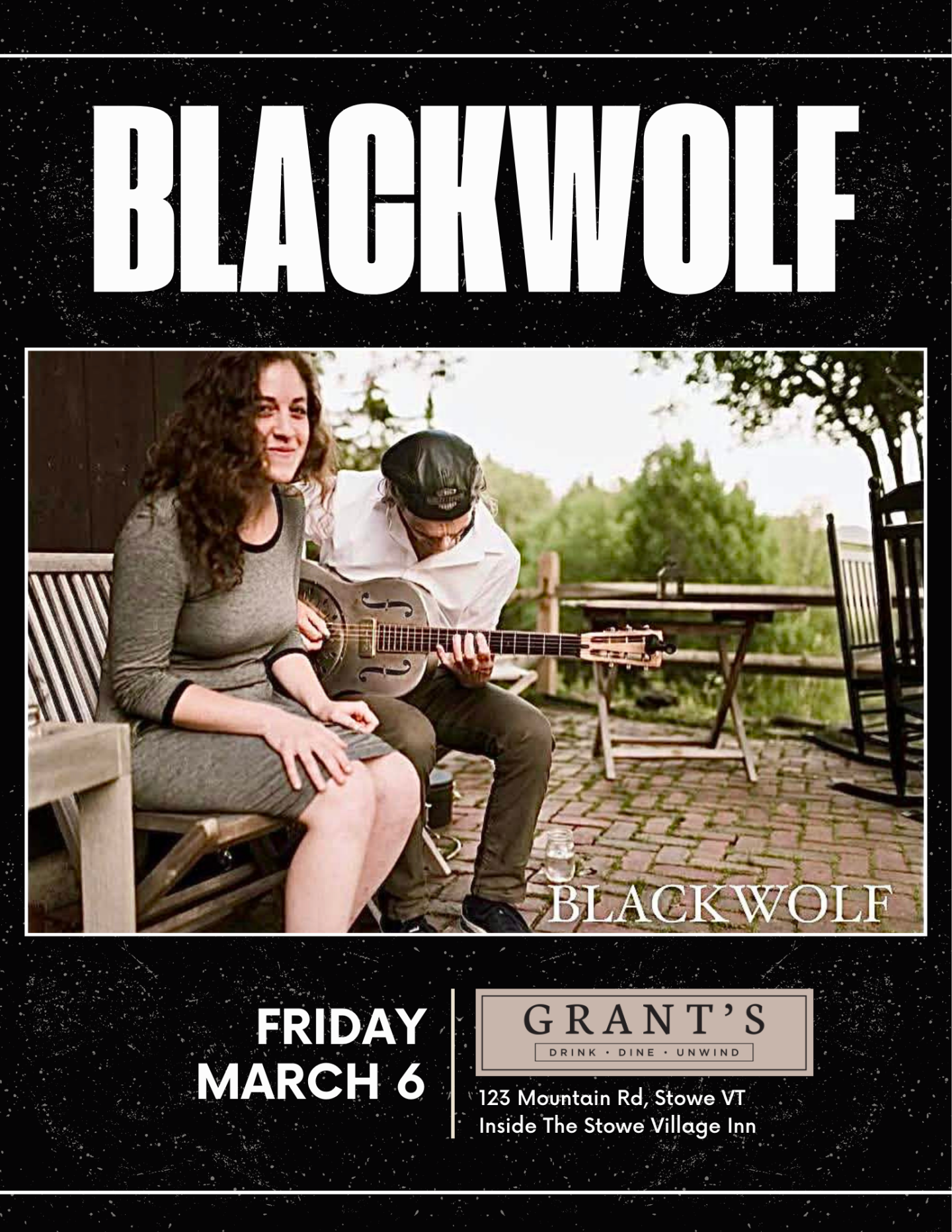 Two musicians on a patio, one plays guitar, the other smiles, greenery in the background.