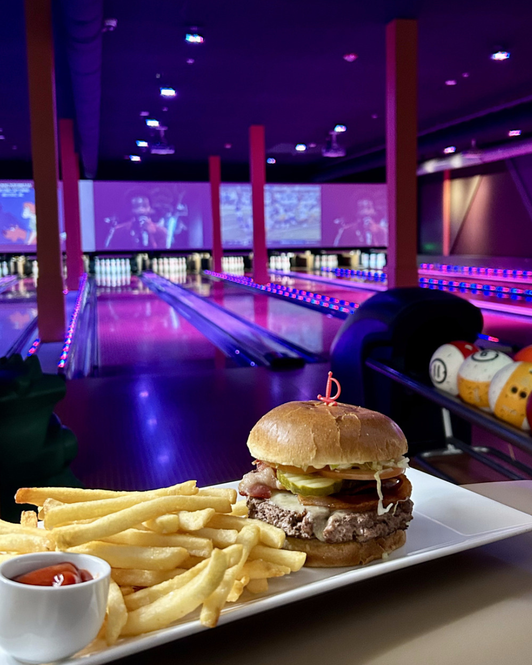 Burger and fries on a table in a bowling alley with neon lights.