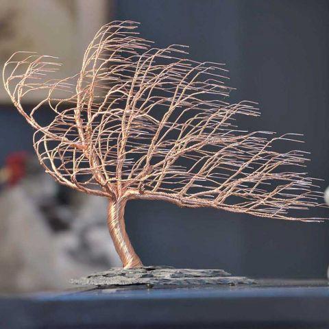 Wire tree sculpture on a rock base with a wind-swept appearance.