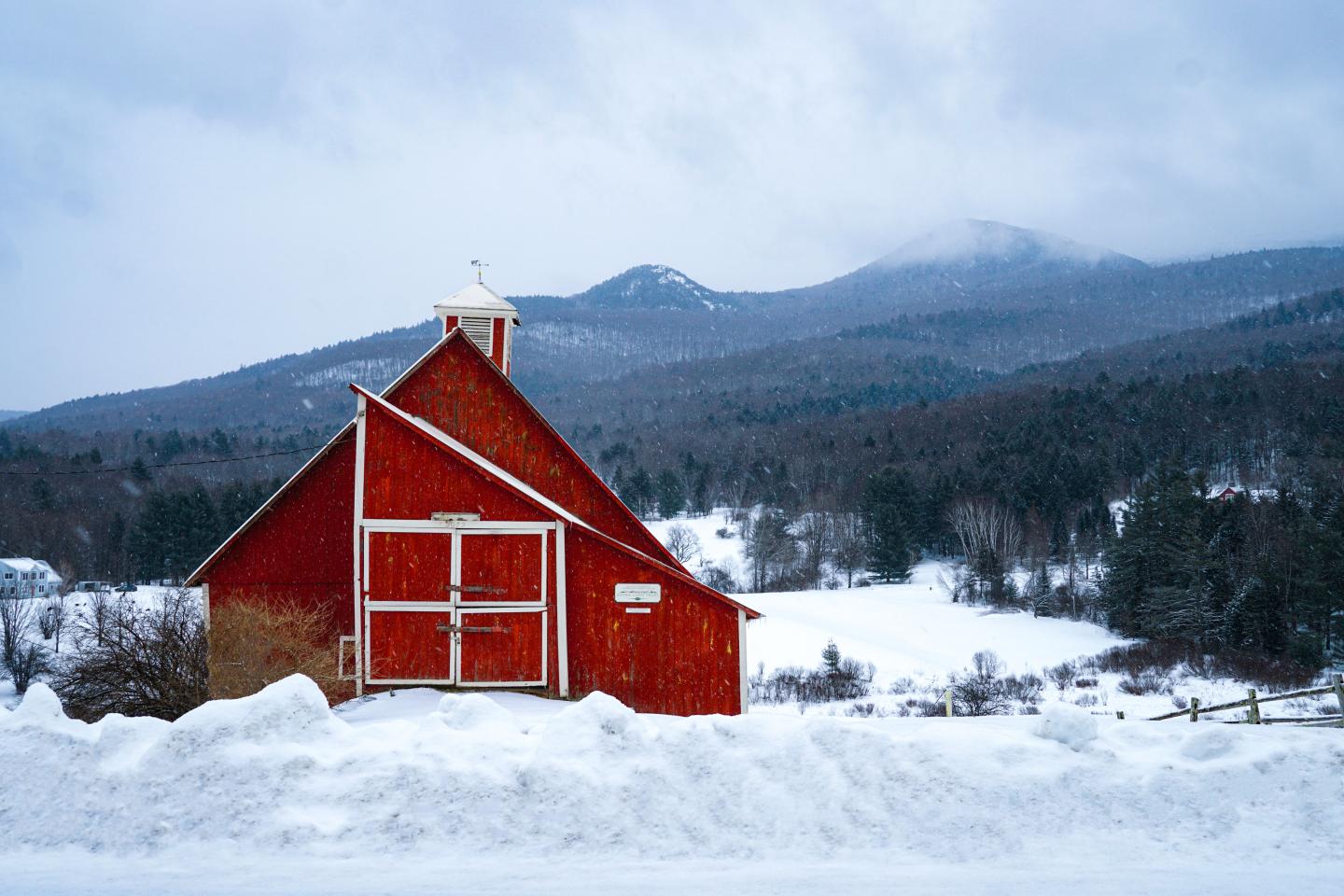 Red barn in snowy landscape with mountains in the background.