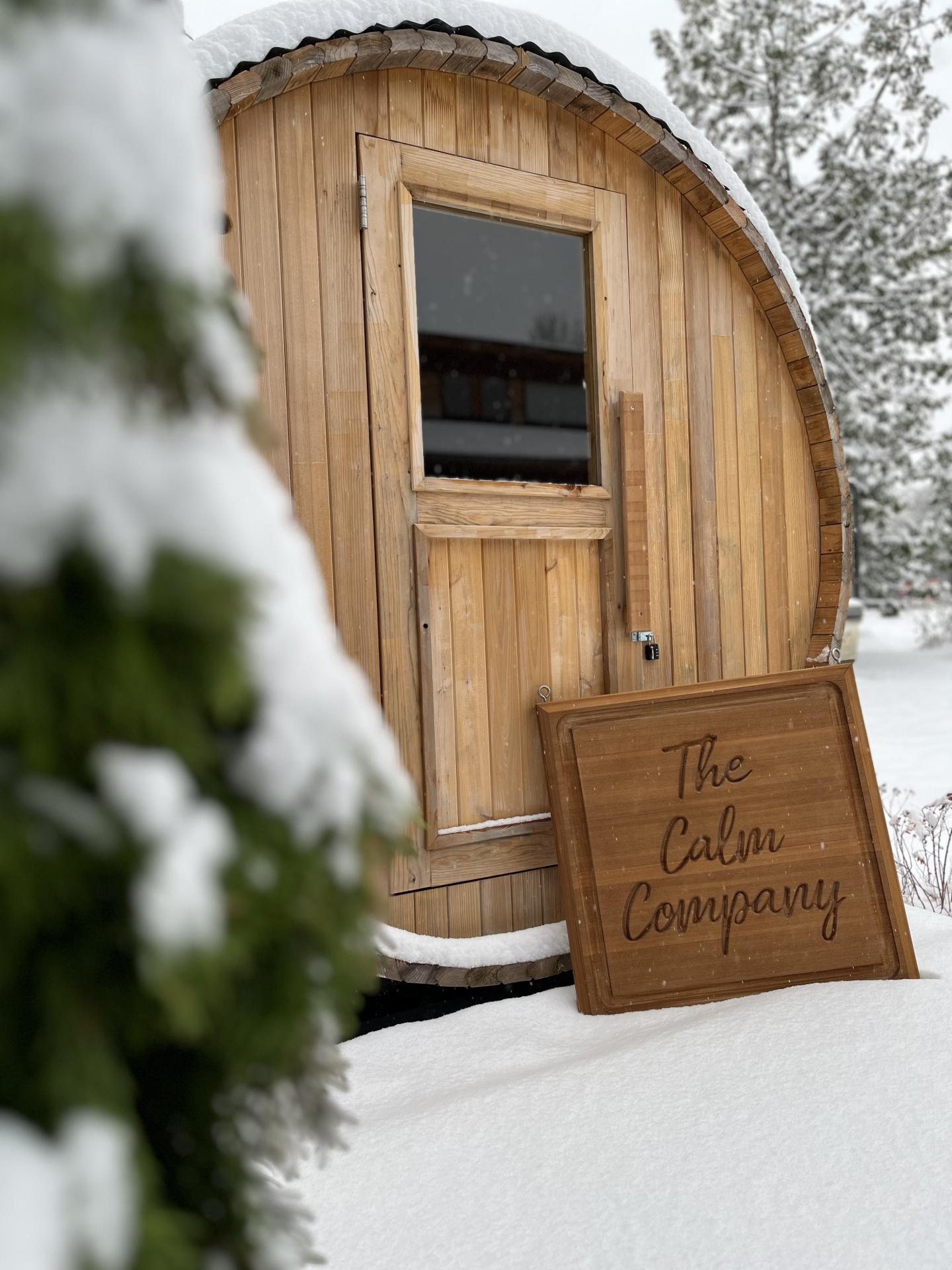 Round wooden sauna in snowy landscape with pine trees.