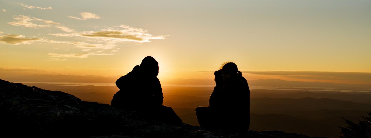 Two people silhouetted against a sunset on a mountain.