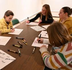 Four people drawing on papers at a table, using markers.