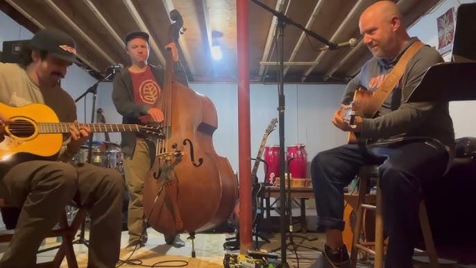 Musicians jam with guitars and upright bass in a cozy basement setting.