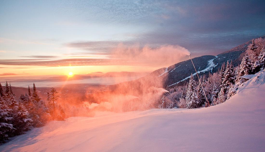 Snowy mountain landscape at sunrise, with trees and a colorful sky.