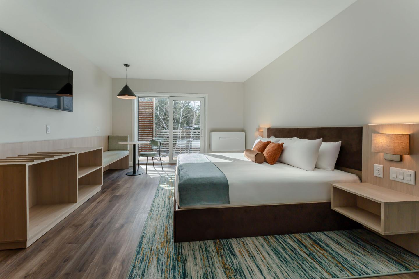 Modern hotel room with a large bed, TV, and sliding glass doors leading outside.