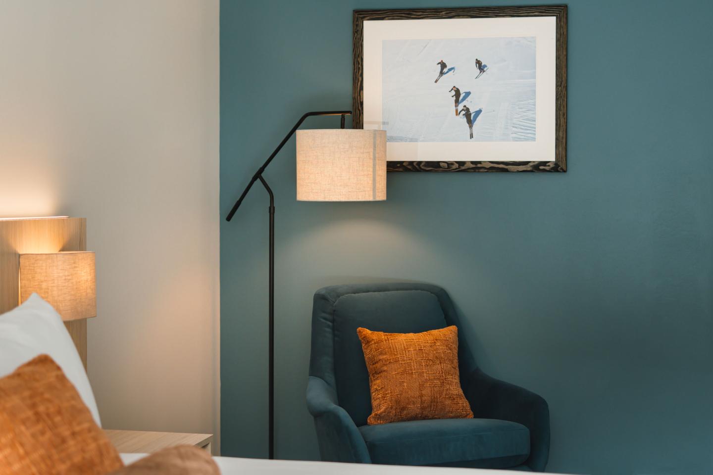 Cozy room with teal chair, orange pillow, and framed art on the wall.