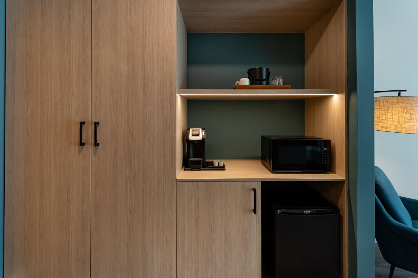 Small kitchenette with coffee maker, microwave, and mini fridge in wood cabinet.