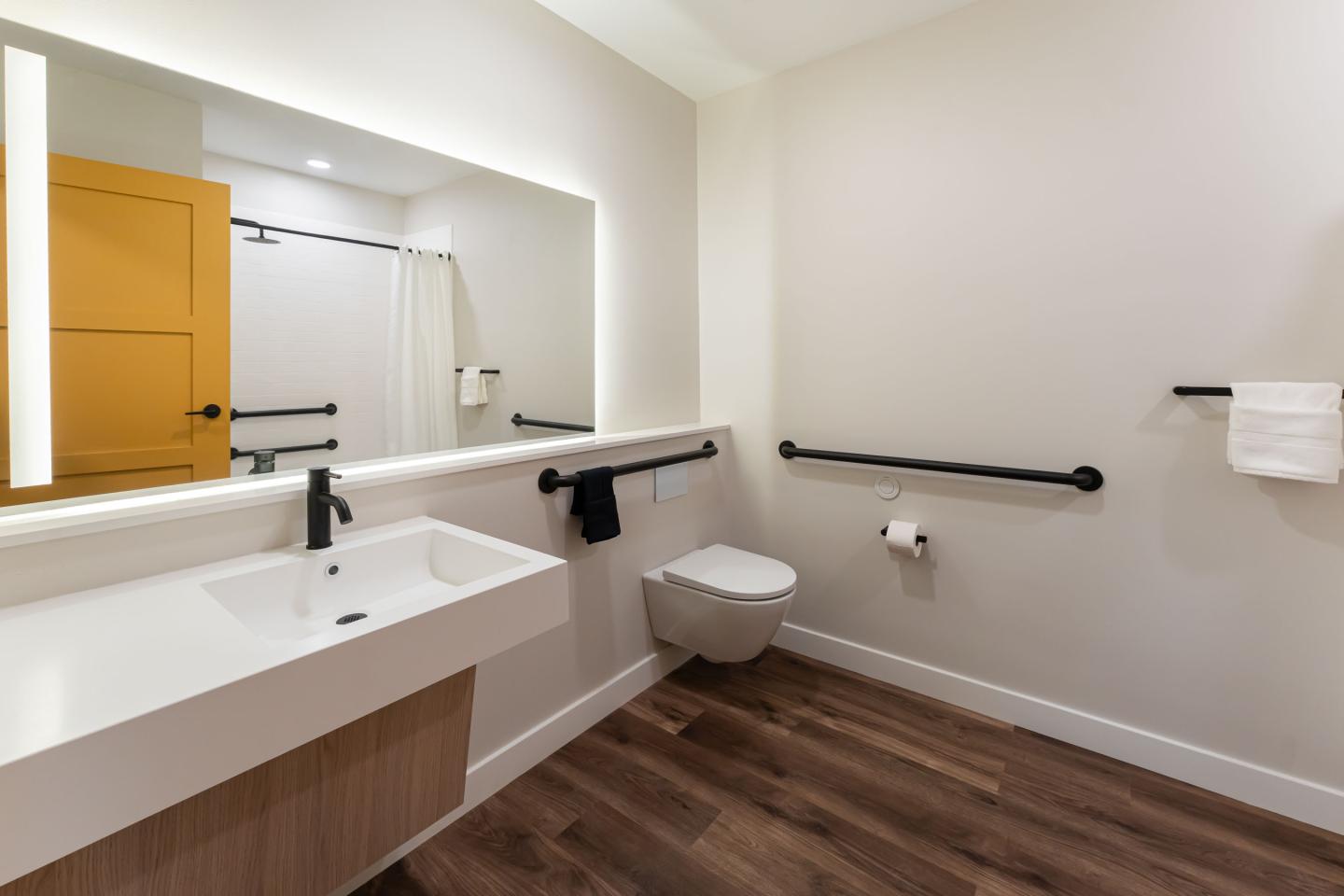 Modern bathroom with accessible features, wood floor, and a large mirror.