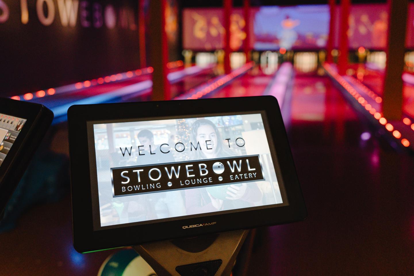 Tablet screen at a bowling alley entrance, vibrant lanes in background.