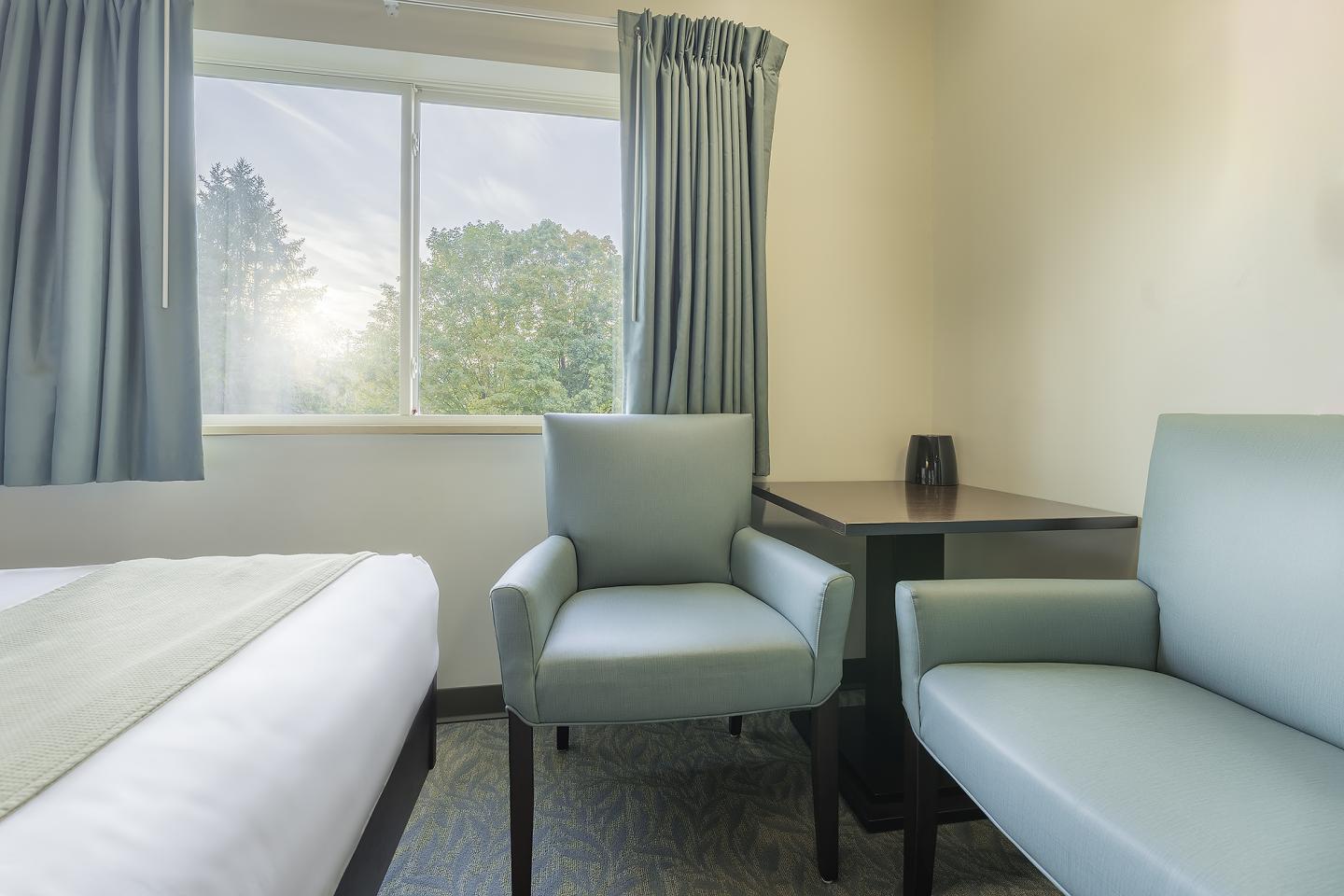 Cozy hotel room with two armchairs, desk, bed, and window with sunlight.