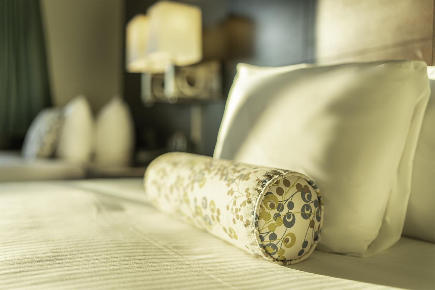 Plush bed with floral bolster pillow and soft lighting.