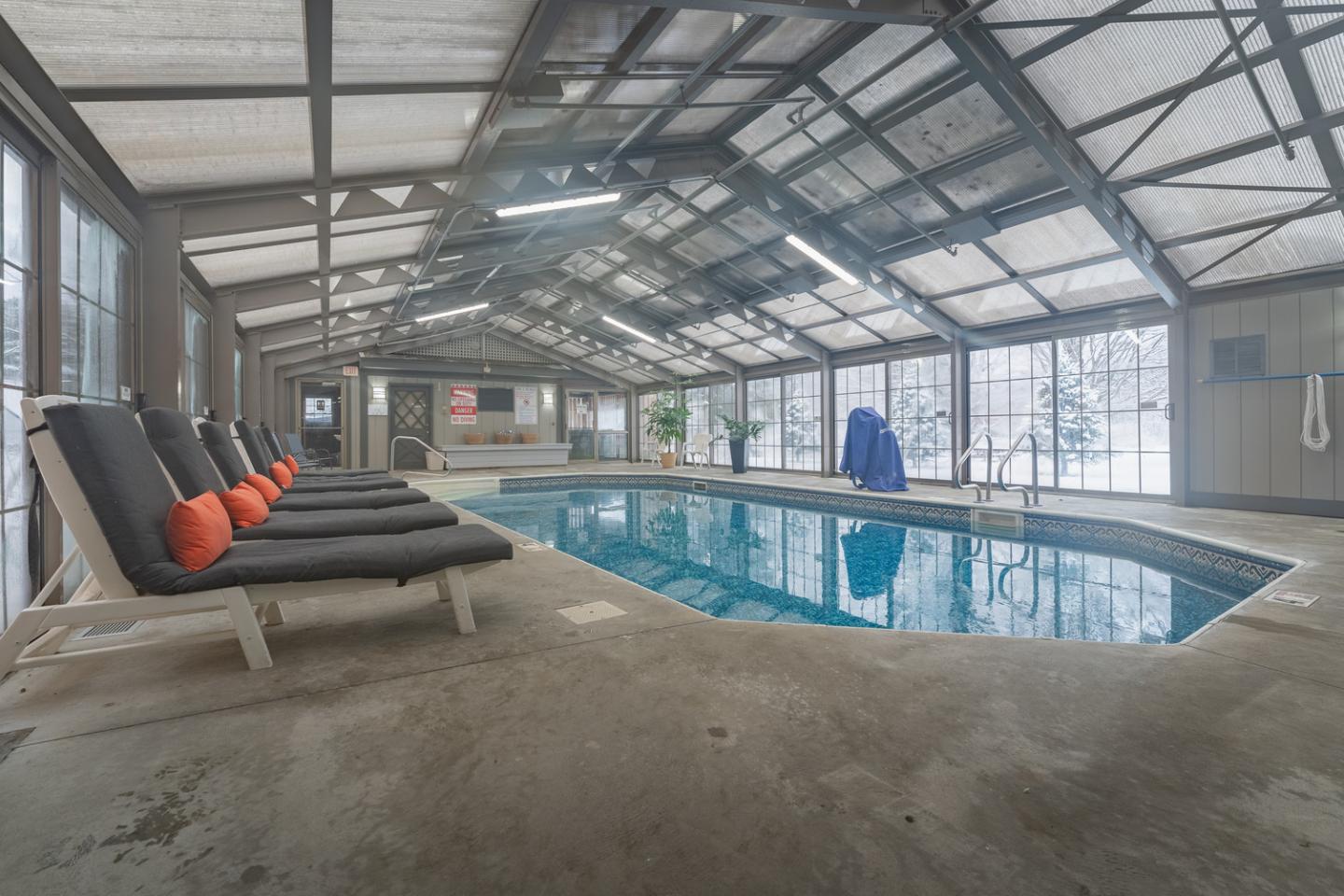 Indoor pool with lounge chairs and large windows.