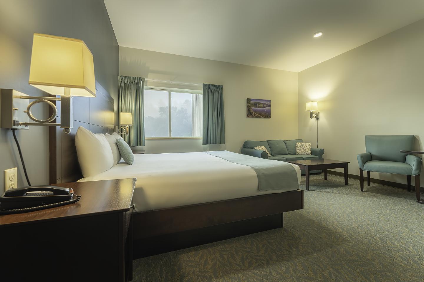 Cozy hotel room with a large bed, sofa, and armchair, softly lit by lamps.