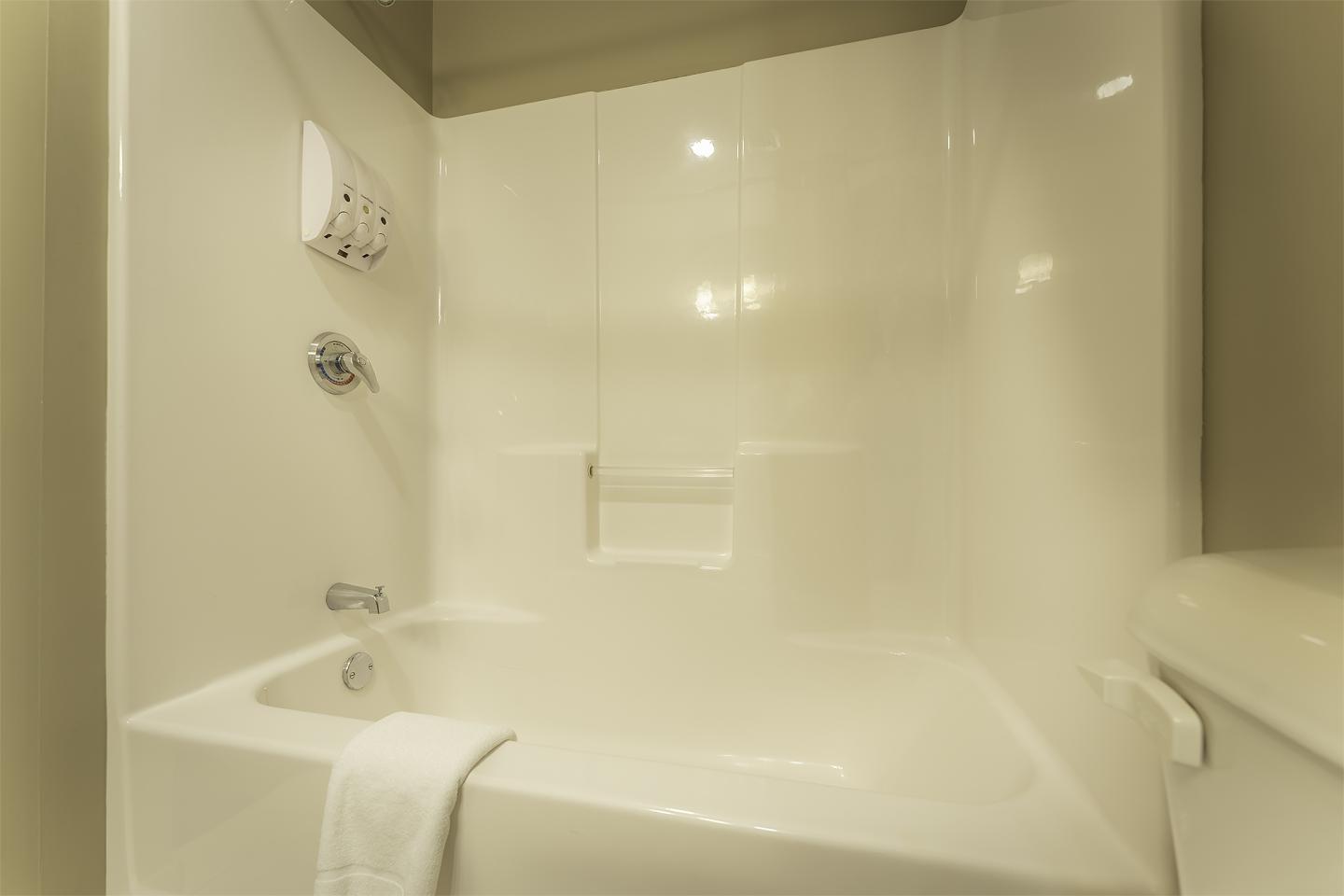 Cream bathroom with bathtub, towel draped over the edge.