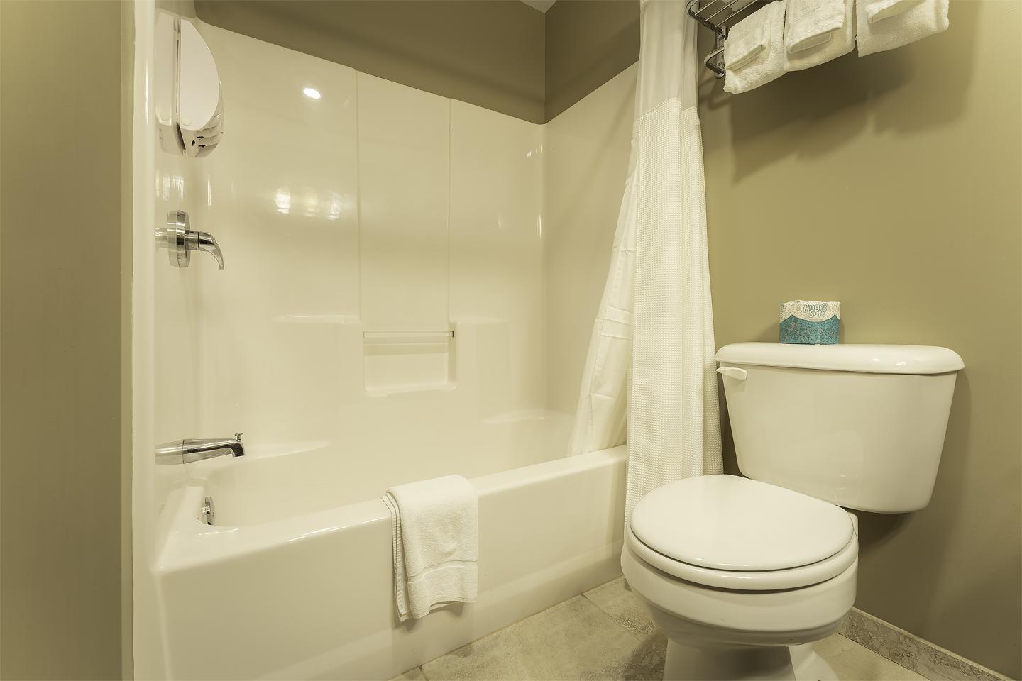 Bathroom with bathtub, curtain, toilet, towel on rack, and beige walls.