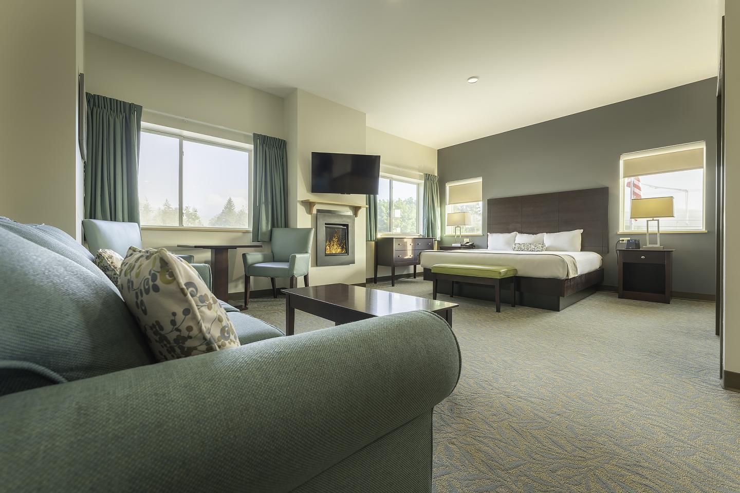 Spacious hotel room with a bed, sofa, fireplace, and large windows.