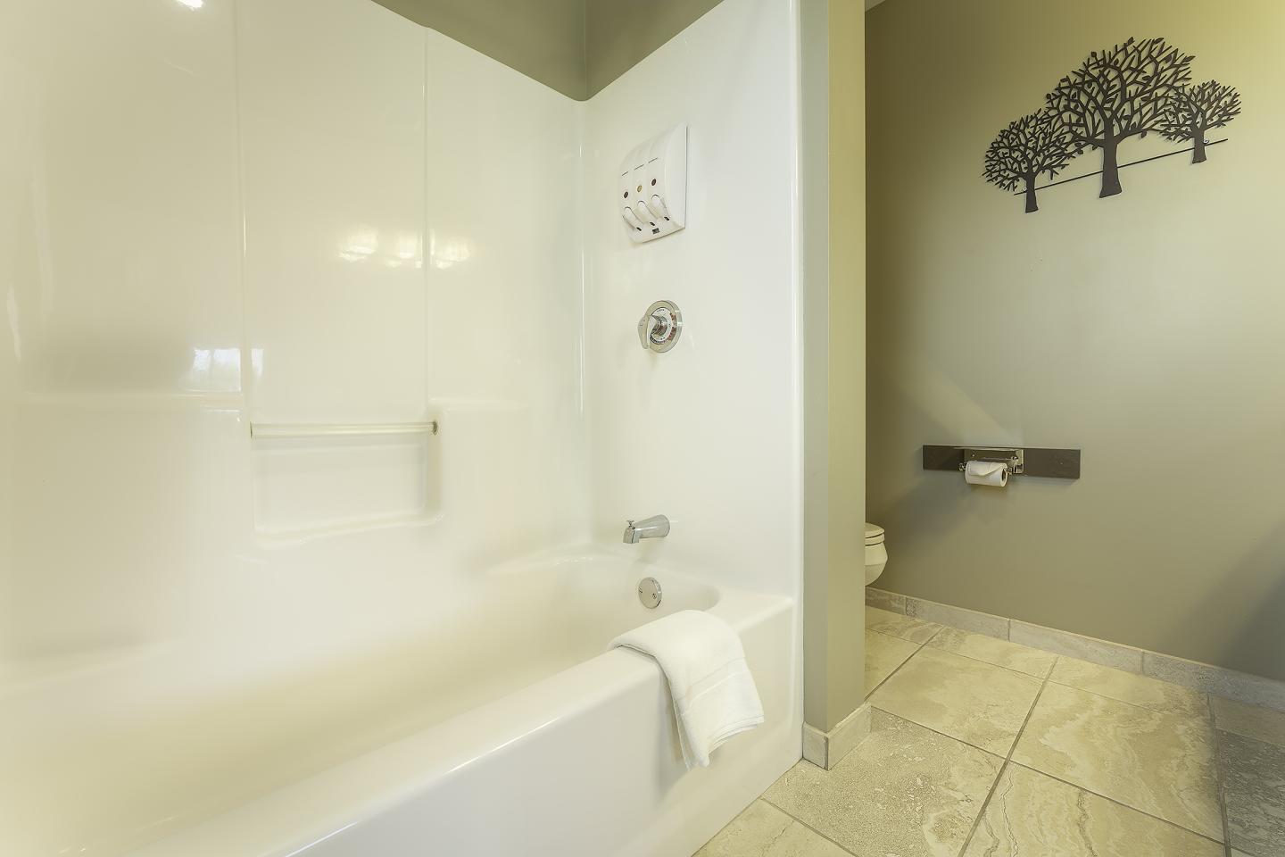 Bathtub with towel, light-colored walls, and tree wall decor.