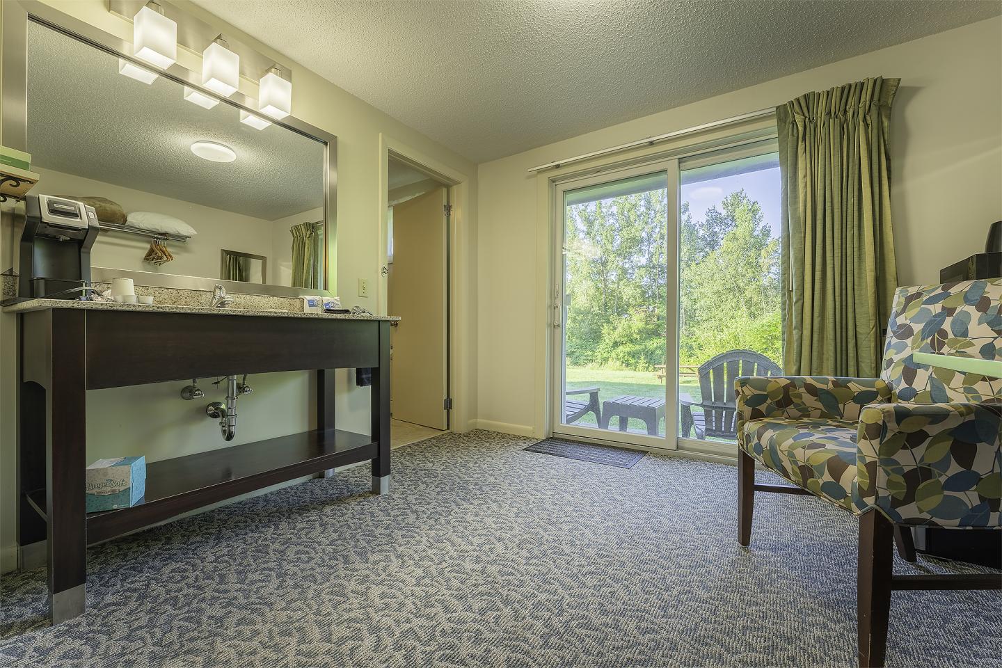 Hotel room with a bathroom sink and sliding glass doors to a patio with chairs.