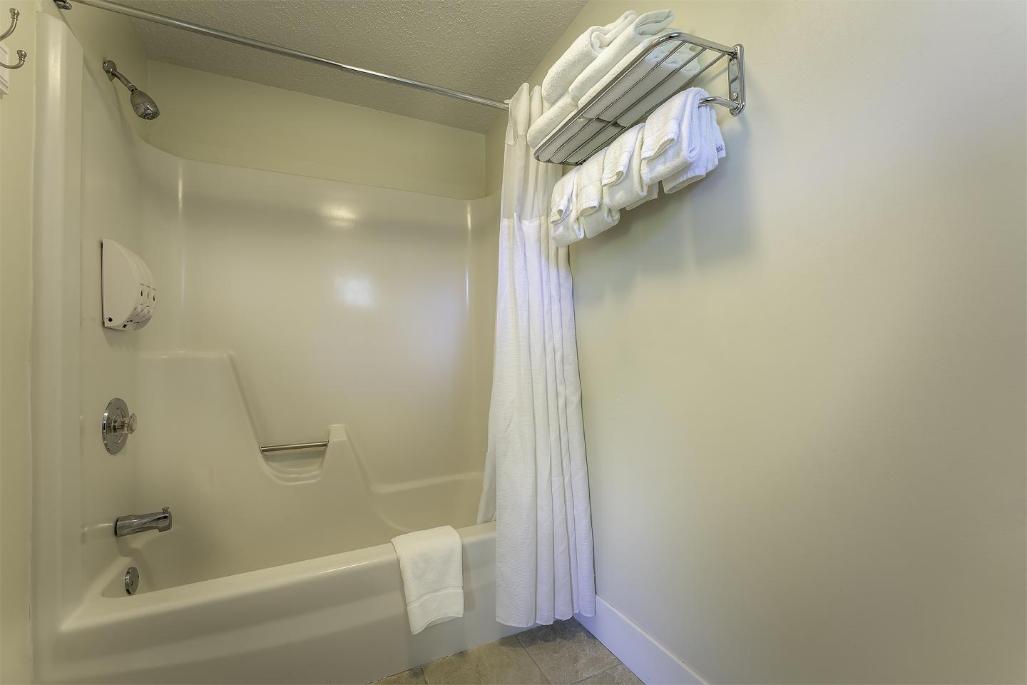 Beige bathroom with bathtub, shower curtain, and towel rack with folded towels.