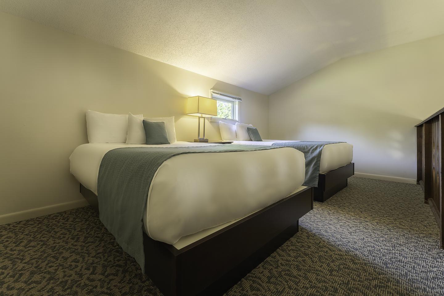 Two neatly made beds in a softly lit bedroom.