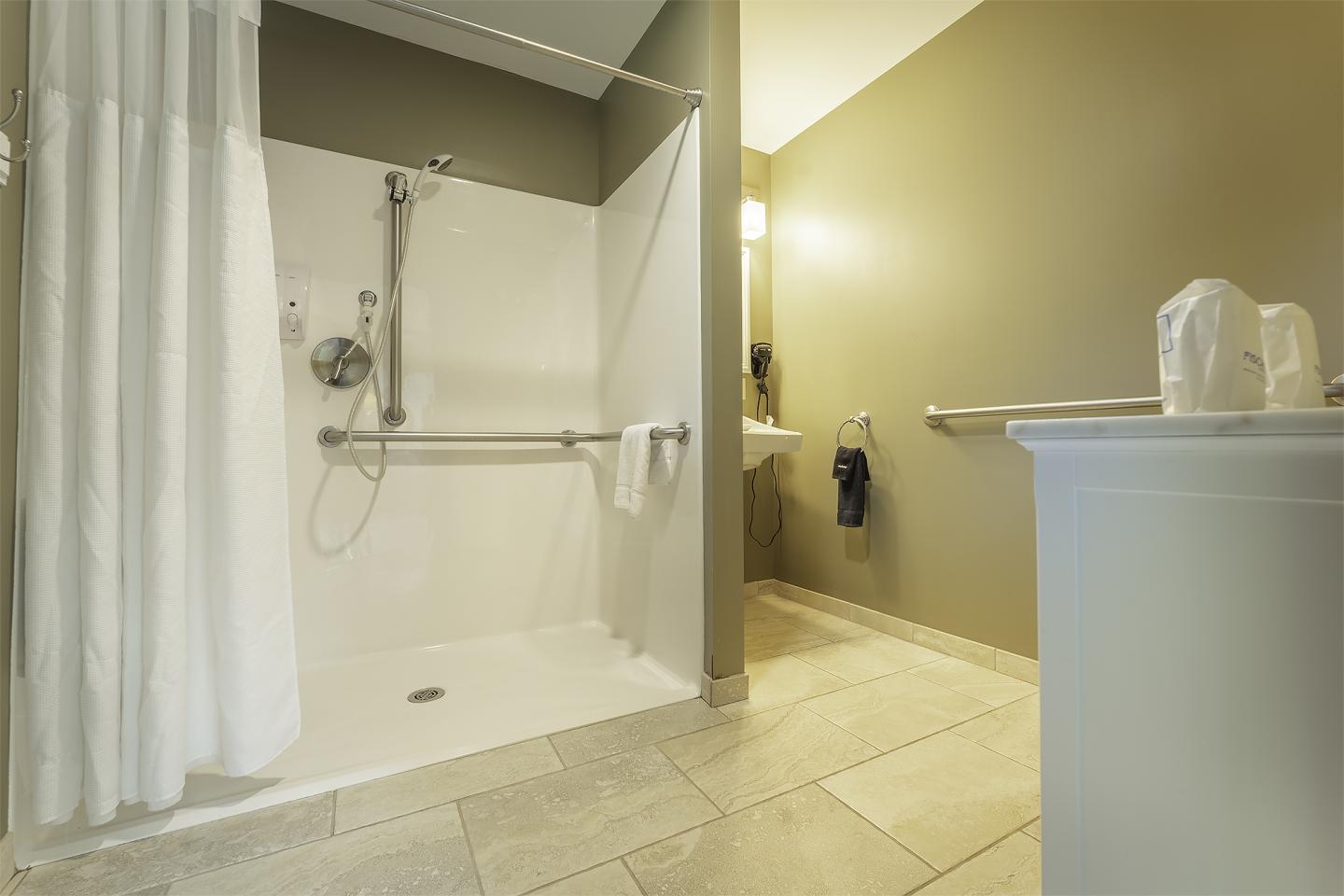Accessible bathroom with shower, grab bars, and beige tiles.